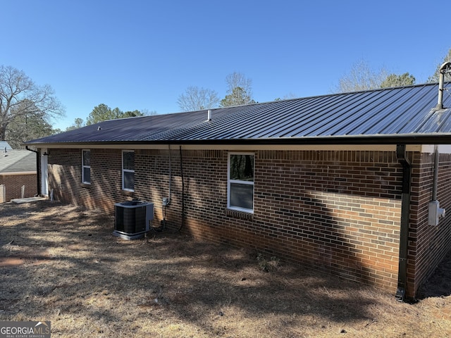 rear view of property featuring a standing seam roof, metal roof, cooling unit, and brick siding