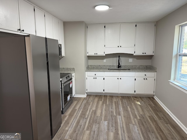 kitchen featuring baseboards, white cabinets, appliances with stainless steel finishes, light stone countertops, and a sink