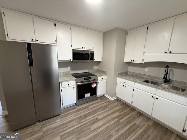 kitchen with light wood finished floors, appliances with stainless steel finishes, light stone counters, white cabinetry, and a sink