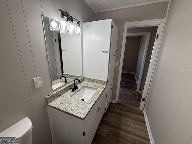 half bath with baseboards, vanity, toilet, and wood finished floors