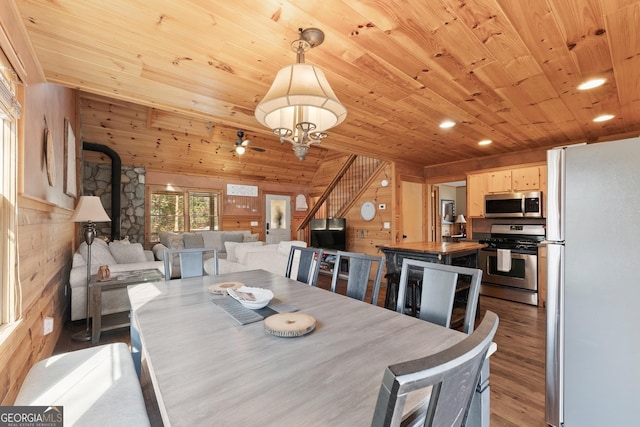 dining room featuring wood ceiling, wood finished floors, a wood stove, stairs, and wood walls