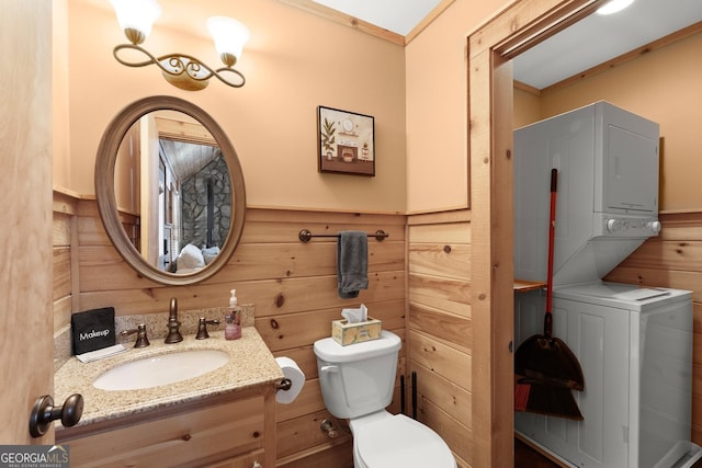 bathroom with toilet, a wainscoted wall, wood walls, stacked washer and clothes dryer, and crown molding