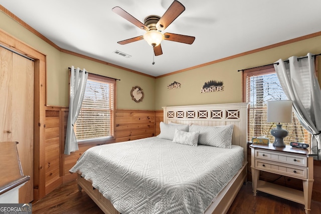 bedroom featuring dark wood-style floors, a wainscoted wall, crown molding, visible vents, and wooden walls