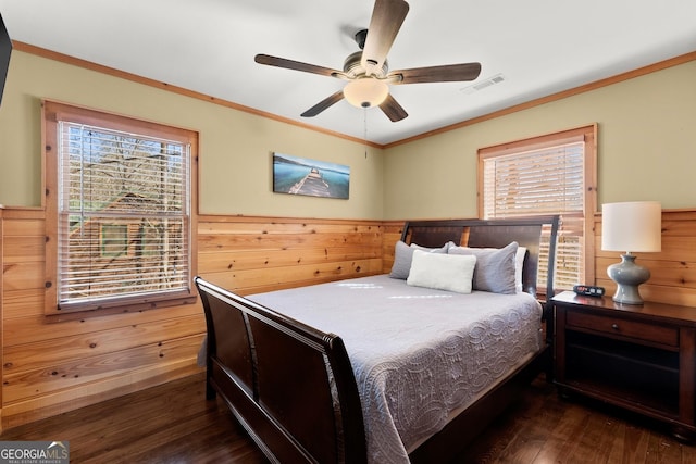 bedroom featuring wooden walls, visible vents, dark wood-style floors, a wainscoted wall, and crown molding