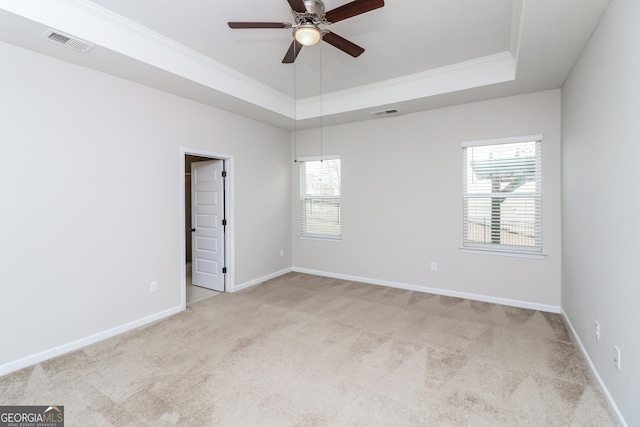 unfurnished room featuring ornamental molding, light colored carpet, a raised ceiling, and visible vents