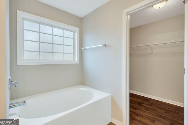 full bath featuring a textured ceiling, a garden tub, wood finished floors, baseboards, and a spacious closet