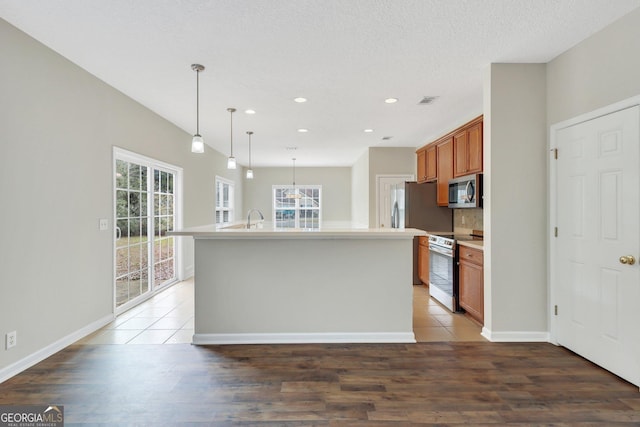 kitchen with pendant lighting, brown cabinets, a center island with sink, light countertops, and appliances with stainless steel finishes