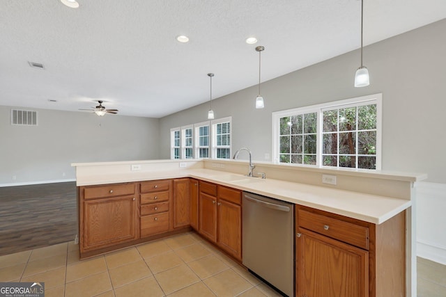 kitchen featuring brown cabinets, decorative light fixtures, light countertops, stainless steel dishwasher, and a sink