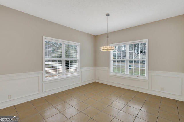 unfurnished dining area with a wainscoted wall and tile patterned floors