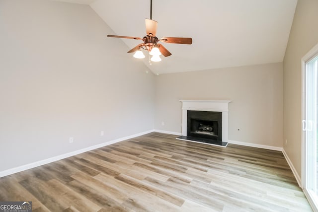 unfurnished living room featuring lofted ceiling, baseboards, a fireplace with raised hearth, and light wood finished floors