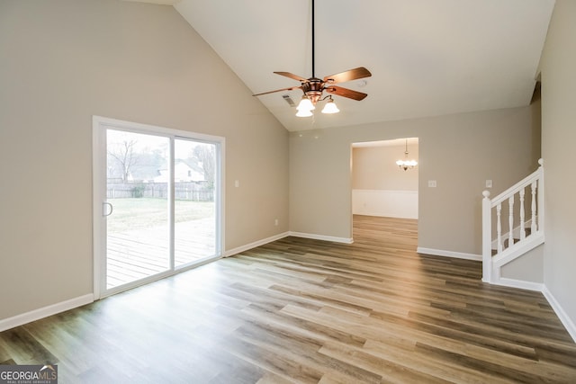 unfurnished living room with stairs, ceiling fan with notable chandelier, wood finished floors, and baseboards