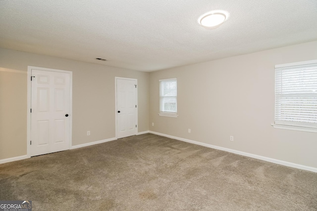 carpeted spare room with visible vents, a textured ceiling, and baseboards