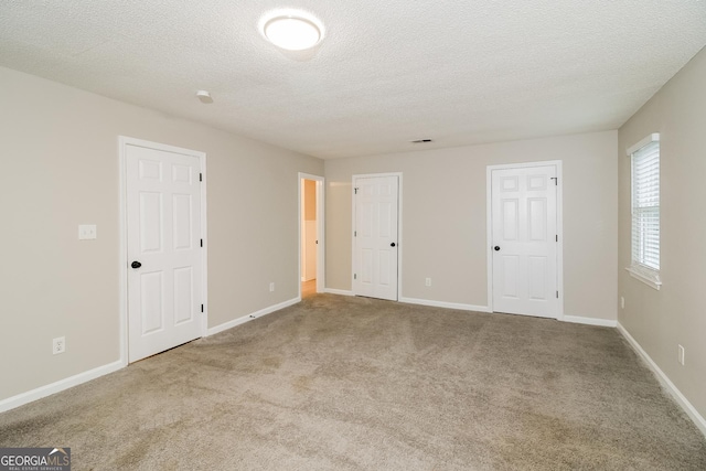 unfurnished bedroom with baseboards, a textured ceiling, visible vents, and light colored carpet