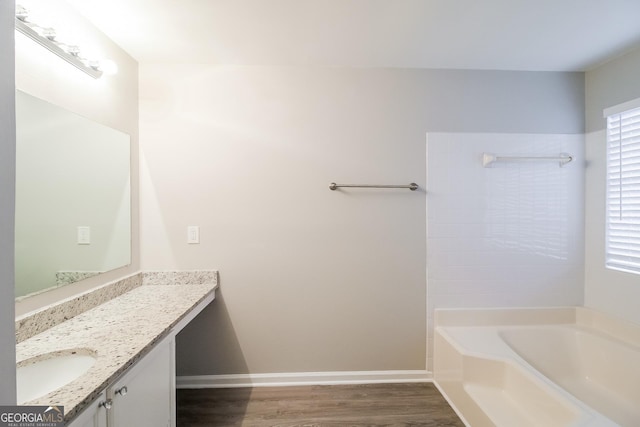 bathroom featuring a bath, wood finished floors, vanity, and baseboards