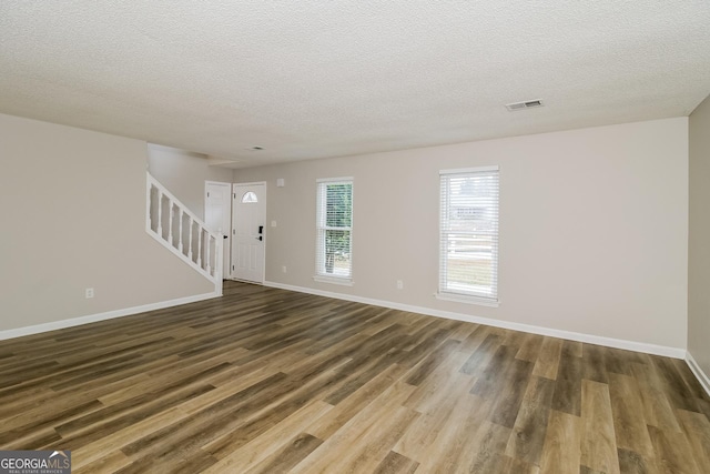 unfurnished living room featuring dark wood-style flooring, visible vents, baseboards, and stairs