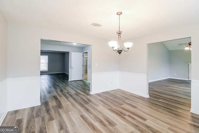 unfurnished room featuring baseboards, visible vents, wood finished floors, and ceiling fan with notable chandelier