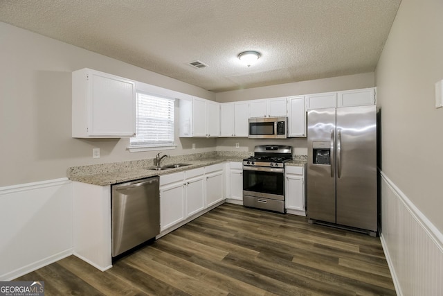 kitchen with dark wood-style flooring, stainless steel appliances, white cabinets, a sink, and light stone countertops