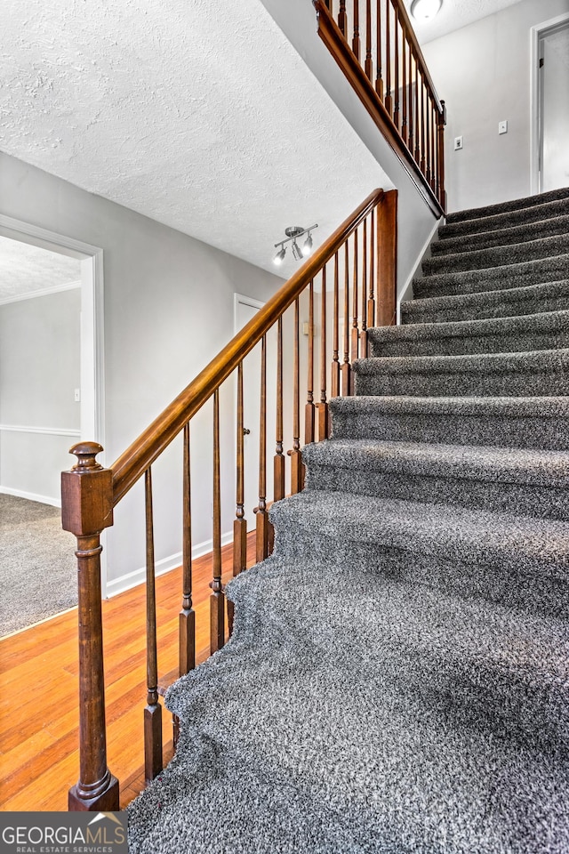 stairway featuring rail lighting, baseboards, a textured ceiling, and wood finished floors