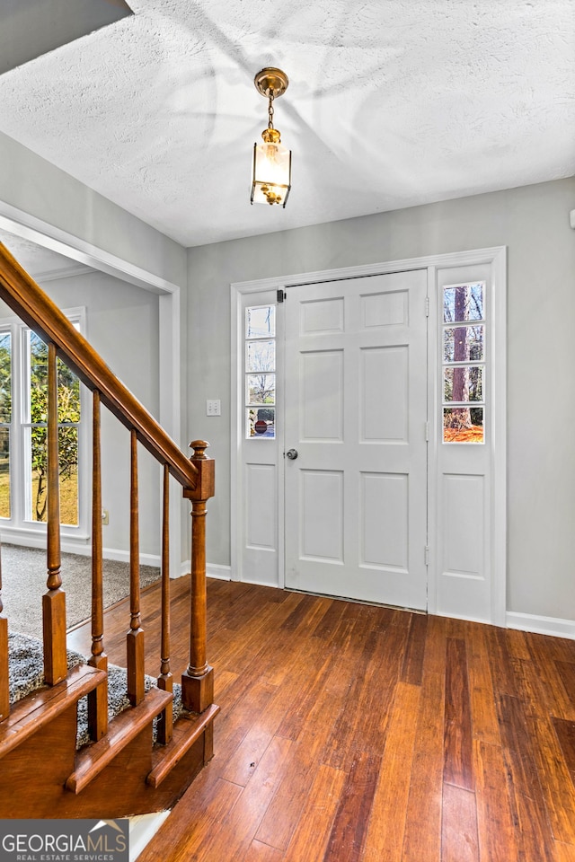 foyer entrance featuring a textured ceiling, dark wood finished floors, stairs, and baseboards