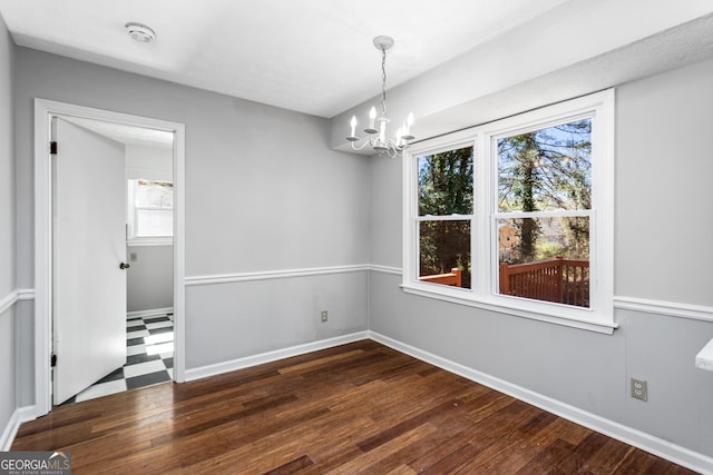 unfurnished dining area with dark wood-type flooring, a notable chandelier, and baseboards