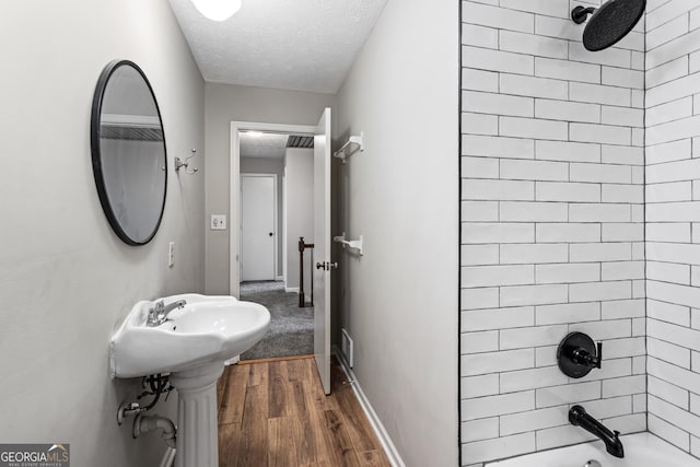 full bath with a textured ceiling, a sink, wood finished floors, baseboards, and washtub / shower combination