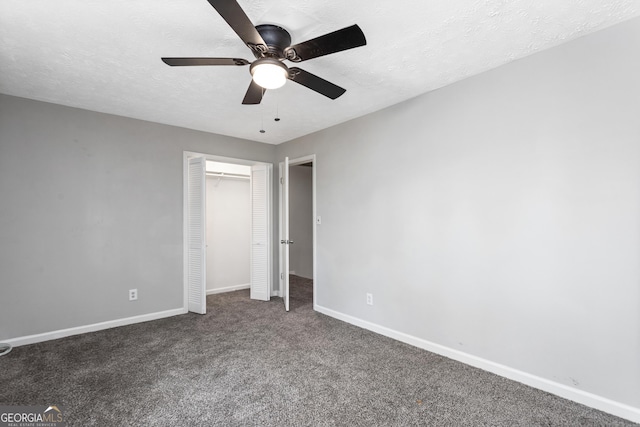 unfurnished bedroom with a textured ceiling, dark colored carpet, a closet, and baseboards