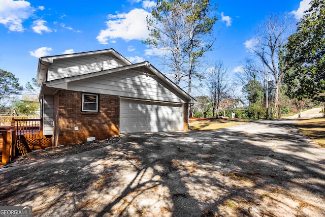 view of property exterior featuring brick siding, an attached garage, crawl space, a deck, and driveway