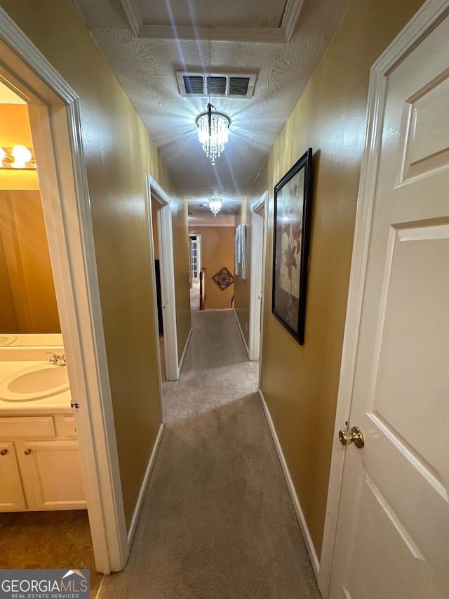 hallway featuring light carpet, visible vents, a sink, and a textured ceiling