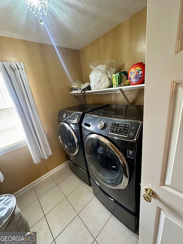 washroom with laundry area, baseboards, a textured ceiling, washing machine and dryer, and light tile patterned flooring