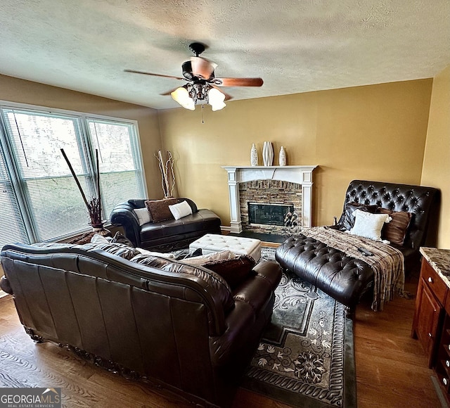 living room with a textured ceiling, a ceiling fan, wood finished floors, and a stone fireplace