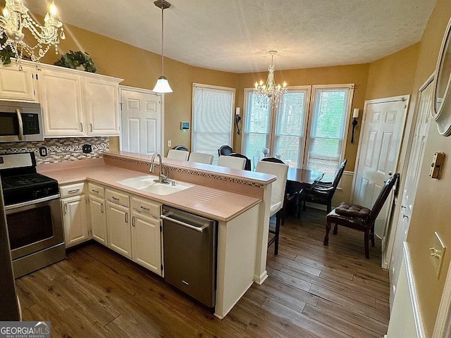 kitchen featuring stainless steel appliances, a sink, white cabinetry, light countertops, and decorative light fixtures