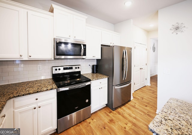 kitchen featuring stainless steel appliances, tasteful backsplash, white cabinetry, light wood-type flooring, and dark stone counters