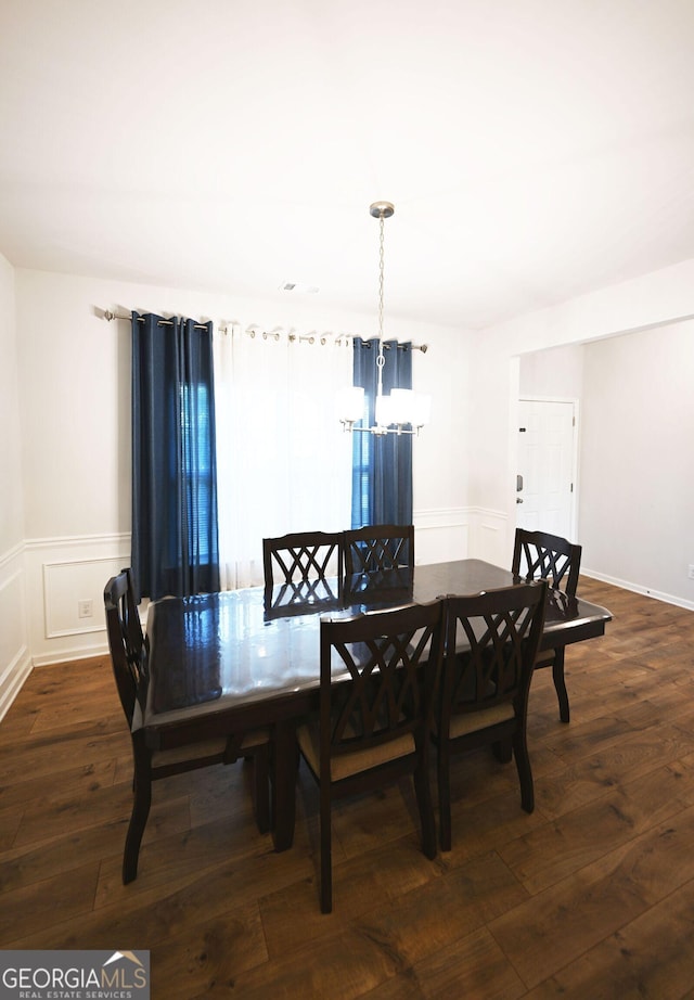 dining space featuring a chandelier, dark wood-style flooring, a wainscoted wall, and a decorative wall