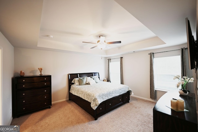 bedroom with light carpet, a raised ceiling, and baseboards