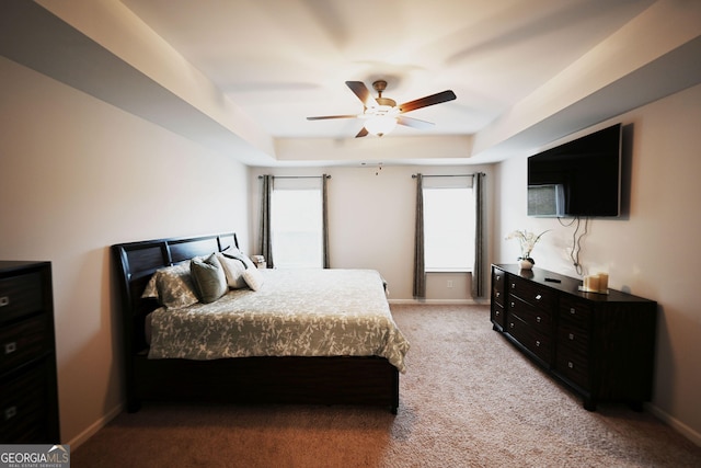 bedroom featuring baseboards, a raised ceiling, a ceiling fan, and light colored carpet