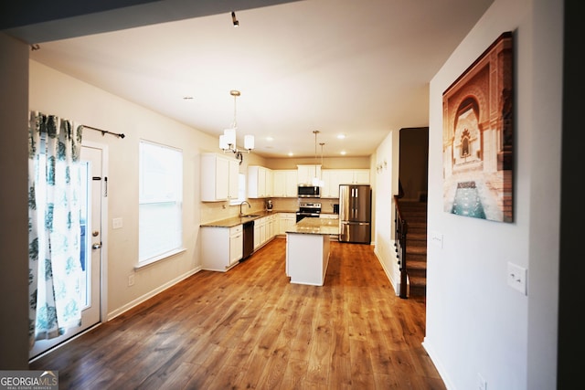 kitchen featuring a kitchen island, hanging light fixtures, stainless steel appliances, white cabinetry, and a sink