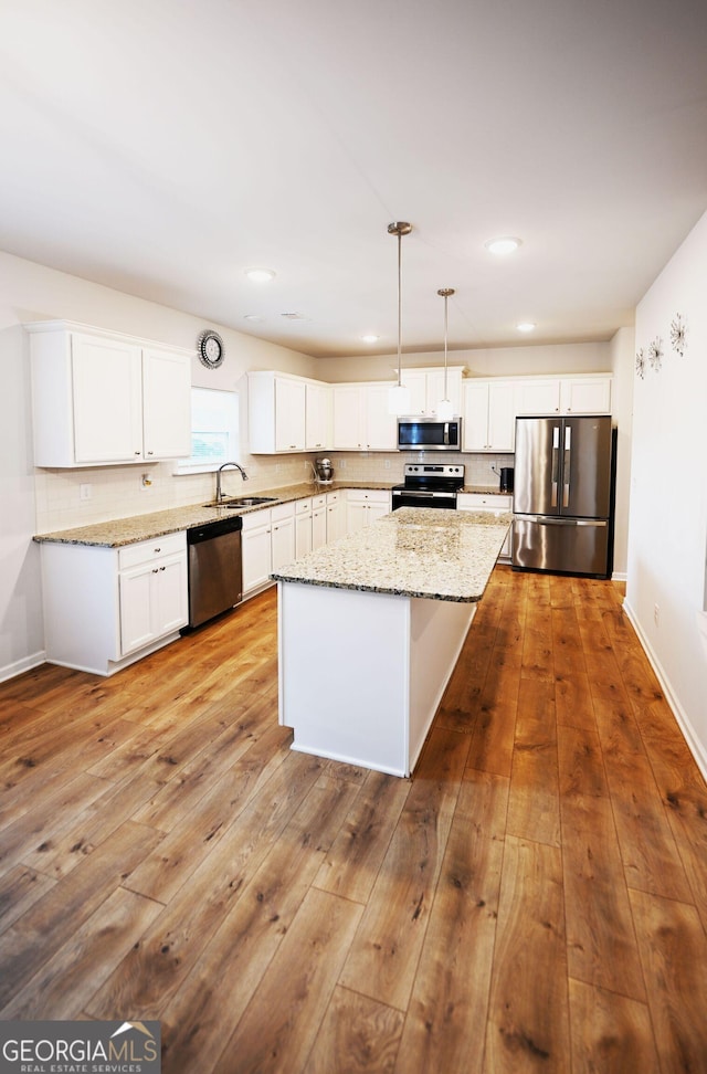 kitchen with light wood finished floors, white cabinets, a kitchen island, decorative light fixtures, and stainless steel appliances