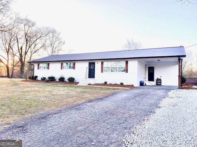 ranch-style home featuring metal roof, driveway, an attached carport, and a front lawn