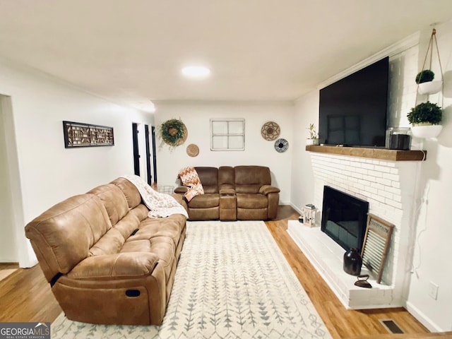 living room featuring a brick fireplace, wood finished floors, visible vents, and baseboards