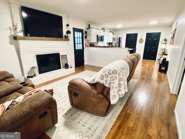 living area featuring recessed lighting, a brick fireplace, baseboards, and wood finished floors