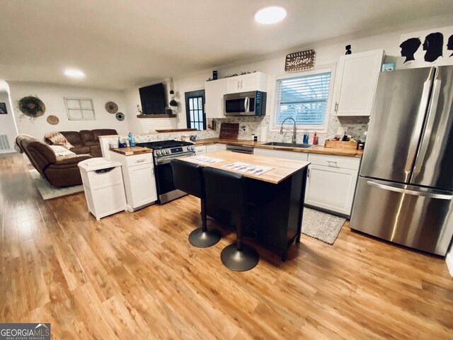 kitchen featuring appliances with stainless steel finishes, open floor plan, a center island, white cabinetry, and a sink