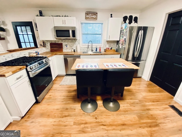 kitchen with a kitchen island, a sink, white cabinetry, appliances with stainless steel finishes, and light wood finished floors