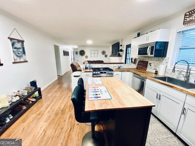 kitchen with butcher block countertops, a peninsula, stainless steel appliances, white cabinetry, and a sink