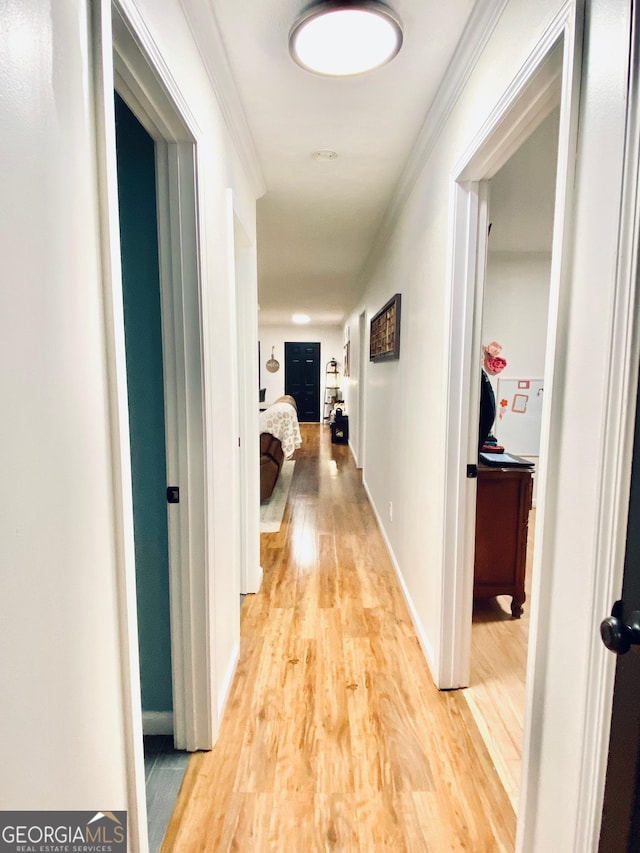 corridor featuring crown molding, light wood-style flooring, and baseboards