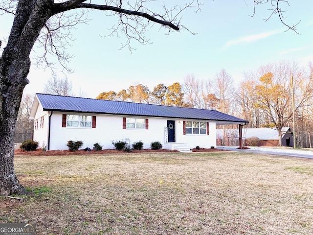 ranch-style house featuring metal roof, an attached carport, a front yard, and brick siding