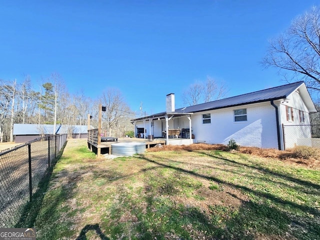 back of house with a chimney, metal roof, fence, a yard, and brick siding