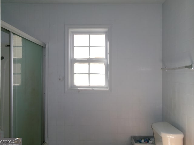 bathroom featuring toilet, a shower with door, and tile walls