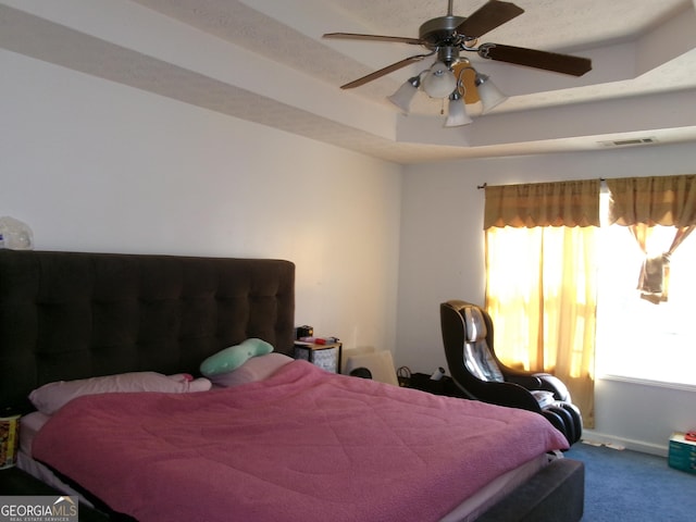 carpeted bedroom with ceiling fan, a raised ceiling, and visible vents