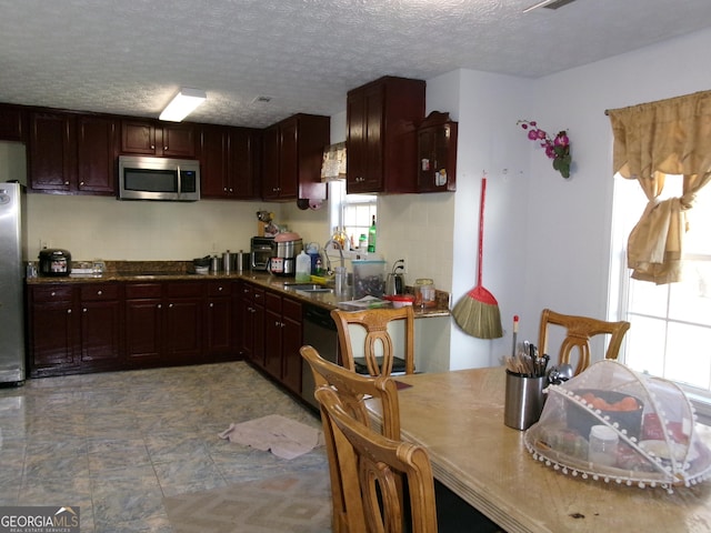 kitchen with a textured ceiling, dark brown cabinetry, a sink, appliances with stainless steel finishes, and dark countertops