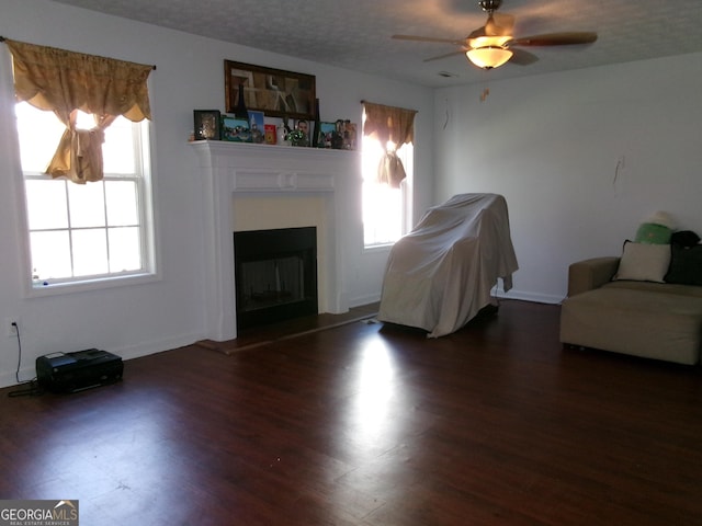 unfurnished living room with a textured ceiling, ceiling fan, dark wood finished floors, baseboards, and a glass covered fireplace